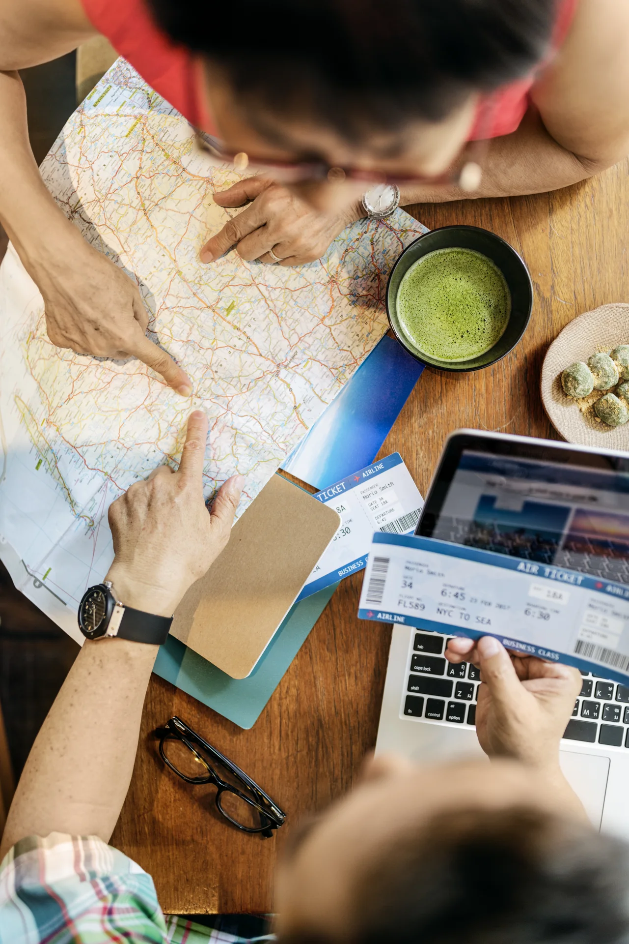 Travellers reviewing a paper map beside a laptop and travel documents.
